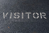 Visitor stencil painted in white on an asphalt parking space