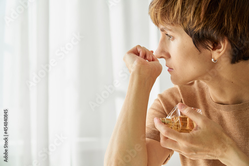 Middle aged woman sniffing perfume bottle. Loss of smell due to coronavirus pandemic. Long-term effect of anosmia and receptor blindness. Concept of covid syndrome. Horizontal shot with copy space photo