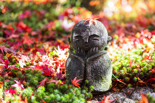 Japanese Jizo sculpture doll with falling Red Maple leaf in Japanese Garden. Landmark and famous in Autumn season © Jo Panuwat D