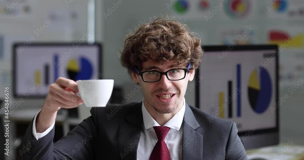 Smart hipster confident adult caucasian businessman positive look sitting in office pay attention listen to speaker in online meeting and raise coffee cup to camera invite to cheer up and celebrate. Smart hipster confident adult caucasian businessman positive look sitting in office pay attention listen to speaker in online meeting and raise coffee cup to camera invite to cheer up and celebrate.