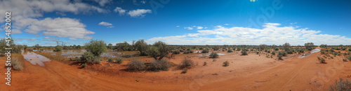 Panoramamic view of the desert in the Australian outback after heavy rain showing large pools of water under a blue sky with whispy clouds