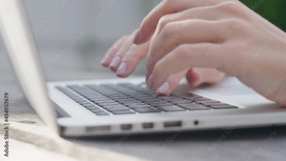 A freelance girl is typing a letter about work on the laptop keyboard. Close-up of a woman's fingers typing on a computer, against the background of a green garden on a sunny day. Work online. A freelance girl is typing a letter about work on the laptop keyboard. Close-up of a woman's fingers typing on a computer, against the background of a green garden on a sunny day. Work online.