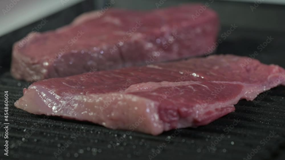 Cooking in the kitchen. The cook puts juicy red raw pieces of fresh veal or beef meat on a hot grill pan for cooking a delicious dinner. Fried steak Cooking in the kitchen. The cook puts juicy red raw pieces of fresh veal or beef meat on a hot grill pan for cooking a delicious dinner. Fried steak