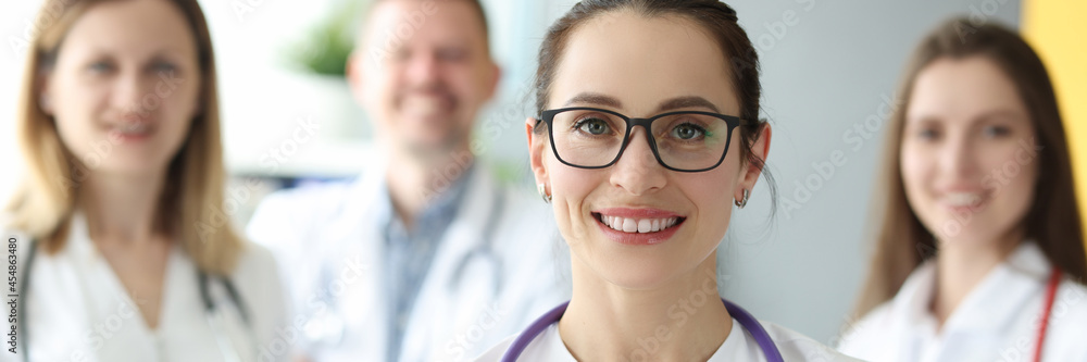Portrait of female doctor in glasses with patient medical history in hands on background of colleagues Portrait of female doctor in glasses with patient medical history in hands on background of colleagues