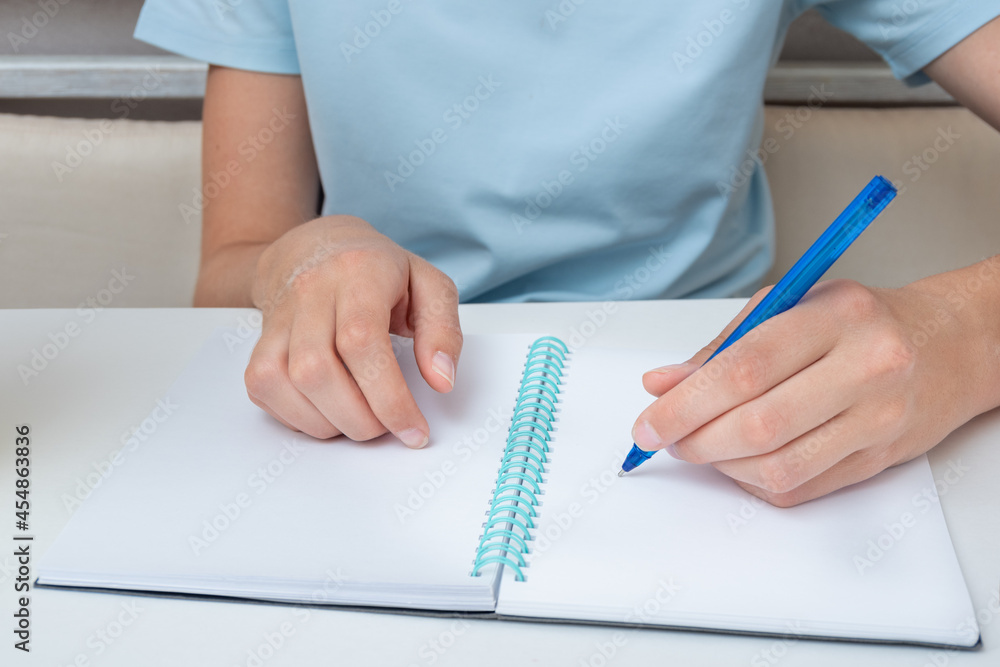 Female student hand holding a pen writing in a notebook, close-up, copy space. Business woman makes a note Female student hand holding a pen writing in a notebook, close-up, copy space. Business woman makes a note