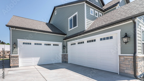 Pano Exterior of a house with concrete driveway and two closed white garage doors with windows