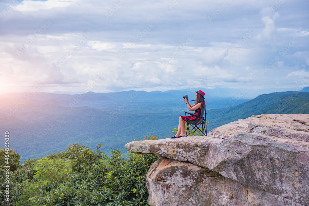A beautiful tourist girl sitting on top of the mountain and taking a picture of valley. Sut Phaendin Cliff, Chaiyaphum, Thailand