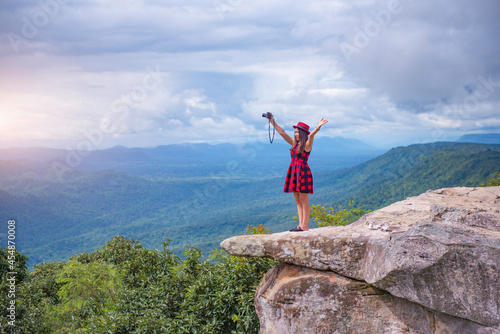 A beautiful tourist girl standing on top of the mountain and taking a picture of valley. Sut Phaendin Cliff, Chaiyaphum, Thailand