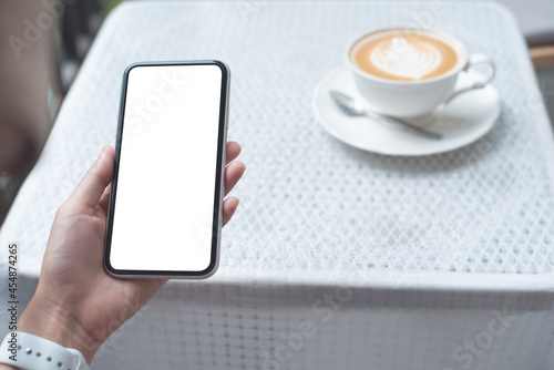 Cell phone mockup image blank white screen. Woman hand holding, using mobile phone at coffee shop.