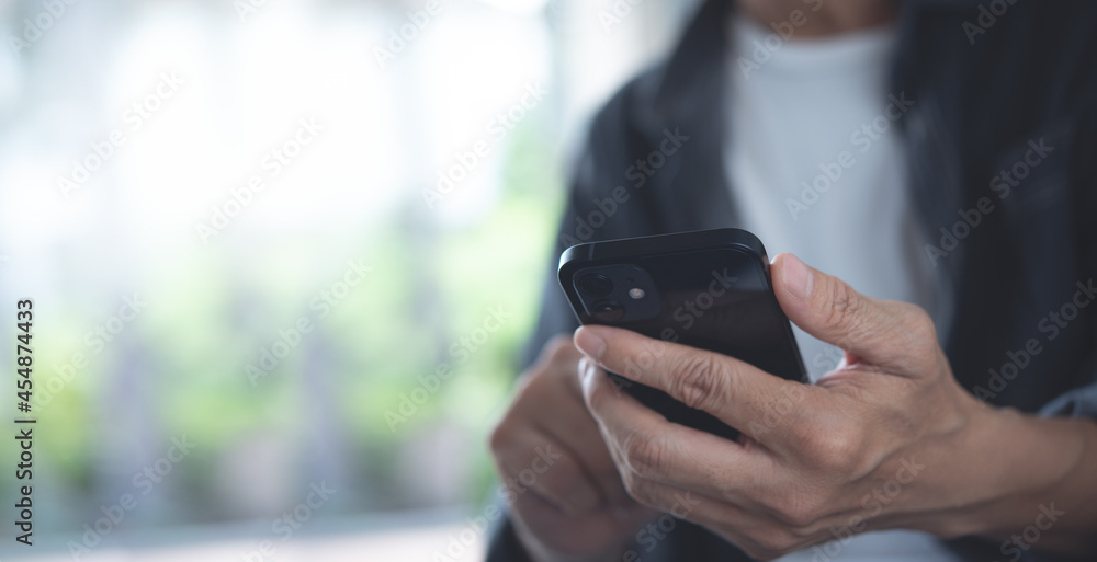 Close up of man in casual wear hands holding, using mobile phone, chatting via mobile apps with blurred background