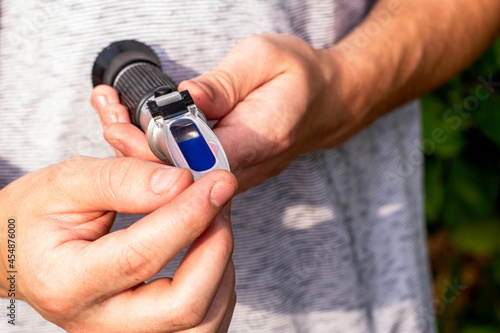 the grower holds a refractometer in his hands to determine the amount of sugar in grape juice