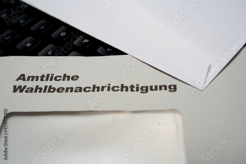 Black letters on white envelope saying: Official election notification (german: Amtliche Wahlbenachrichtigung). Black keyboard in background. depth of field. 2021 federal election in germany. Closeup. photo