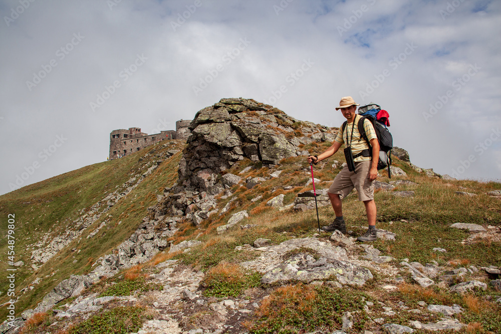 Middle-aged man with a backpack on the background of mountain landscape. Ruins of astronomical observatory called White elephant on the peak - Pip Ivan.
