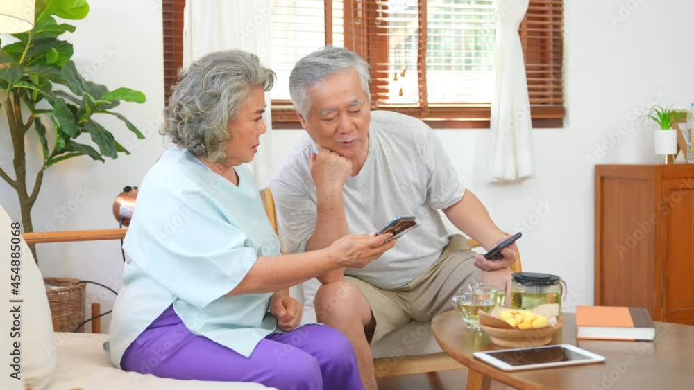Happy Asian elderly family relaxing together at home. Senior couple using smartphone social media or online shopping. Retirement family husband and wife enjoy leisure activity with technology at home Happy Asian elderly family relaxing together at home. Senior couple using smartphone social media or online shopping. Retirement family husband and wife enjoy leisure activity with technology at home