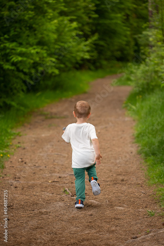 Little boy of 3 years old runs away from the forest path deep into the forest