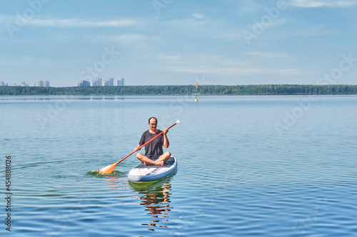 Asian older man on sup board on calm lake.