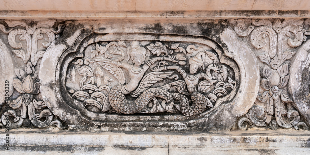 Beautiful ancient bas-relief stucco panel of two mythological half woman half fish creatures on wall of hor trai library in Wat Phra Singh buddhist temple, famous landmark of Chiang Mai, Thailand