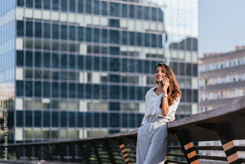 horizontal portrait of a young indian woman talking by phone with offices buildings on the background photo