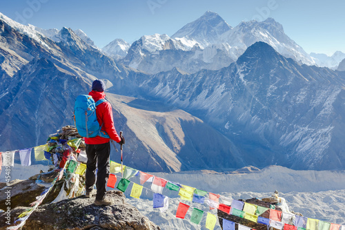 Vászonkép Hiker with trekking poles stands on the slope against the background of high sno