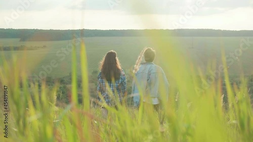 The couple in green field. Summer field with green grass. Two silhouettes in grass field. Romantic date in field. The girl and the boy look to the blue sky. Grass is swaying in the wind.