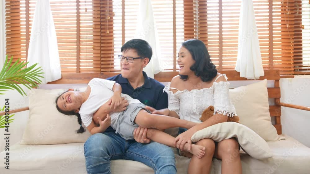Happy Asian family relaxing at home. Smiling parents embracing and playing with little daughter on sofa in living room. Father and mother with cute child girl kid having fun weekend activity together. Happy Asian family relaxing at home. Smiling parents embracing and playing with little daughter on sofa in living room. Father and mother with cute child girl kid having fun weekend activity together.
