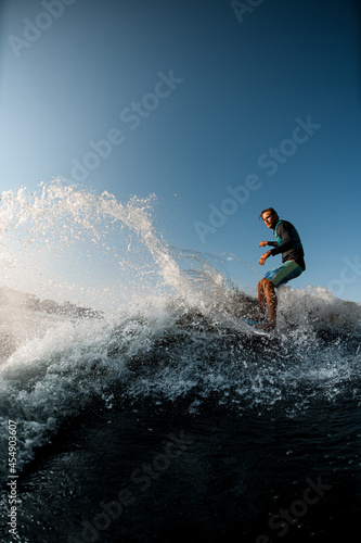 man skilfully riding wave on the wakesurf on the background of blue sky