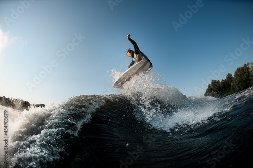 wakesurfer actively jumping on high wave on the background of blue sky