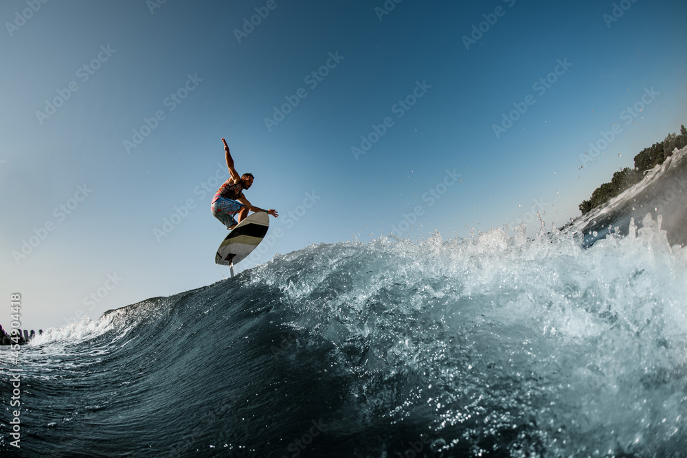 Great view of the splashing wave and man jumping over it on foilboard