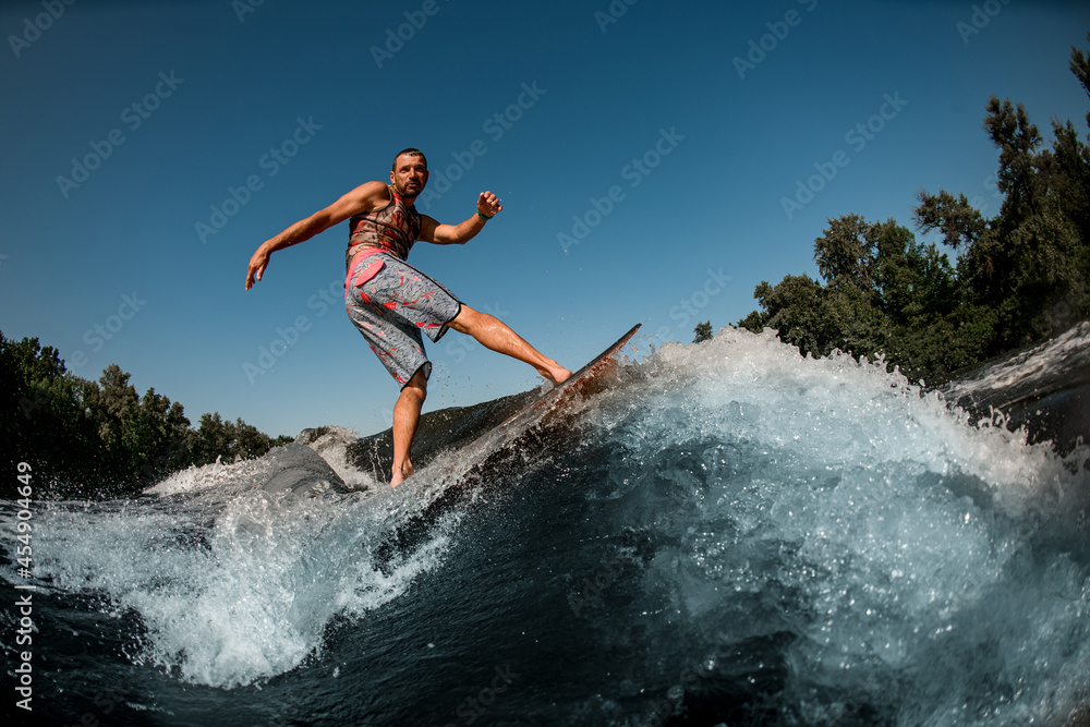 Active guy on foilboard balancing on wave against the background of blue sky.