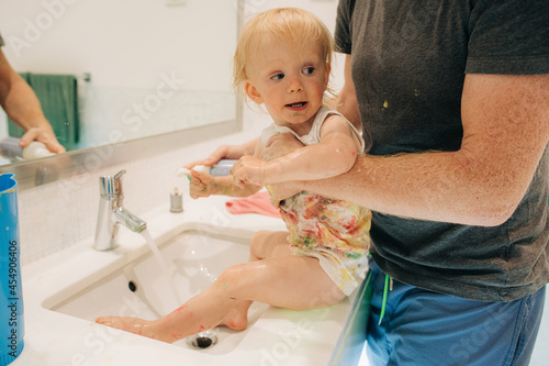 Father washing little girl in bathroom sink. Portrait of messy baby girl in fathers hands. Childcare and hygiene concept