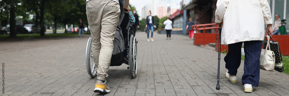 Fototapeta premium Man rolls a seated woman in wheelchair down street in city