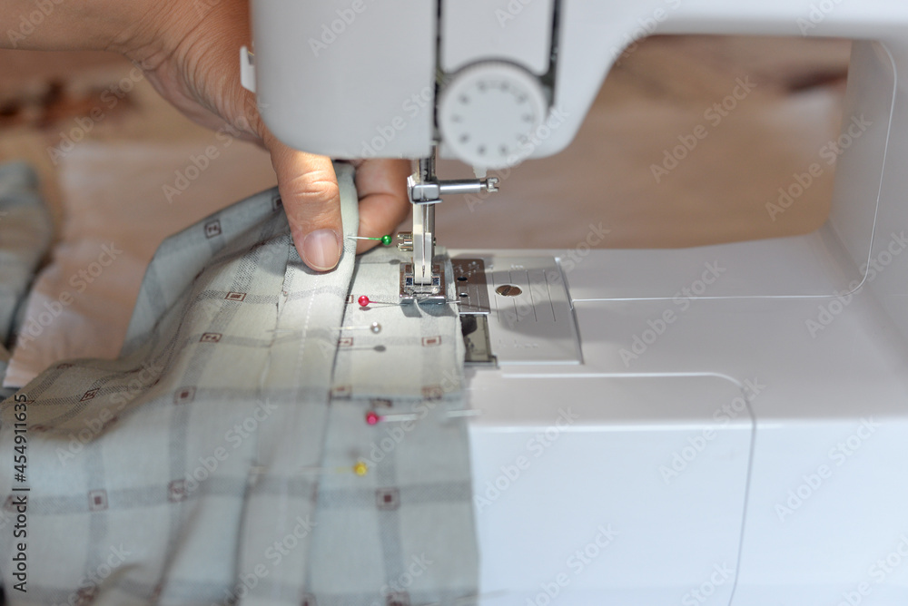 stitching on a sewing machine through tailor's needles, a dressmaker at home sews a silk shirt on a sewing machine.