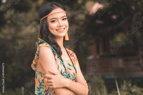 A smiling young teenage woman with cute dimples in an orange and green boho style tropical outfit. Outdoor shot, warm tones. photo