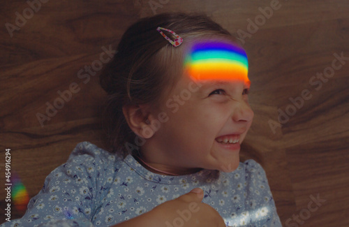 girl lies with her eyes closed and a glare of a rainbow on her face