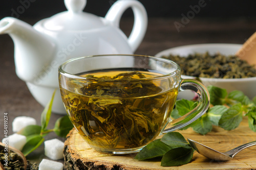 Green tea. Hot tea in a cup on a wooden stand, sugar and mint on a dark background.