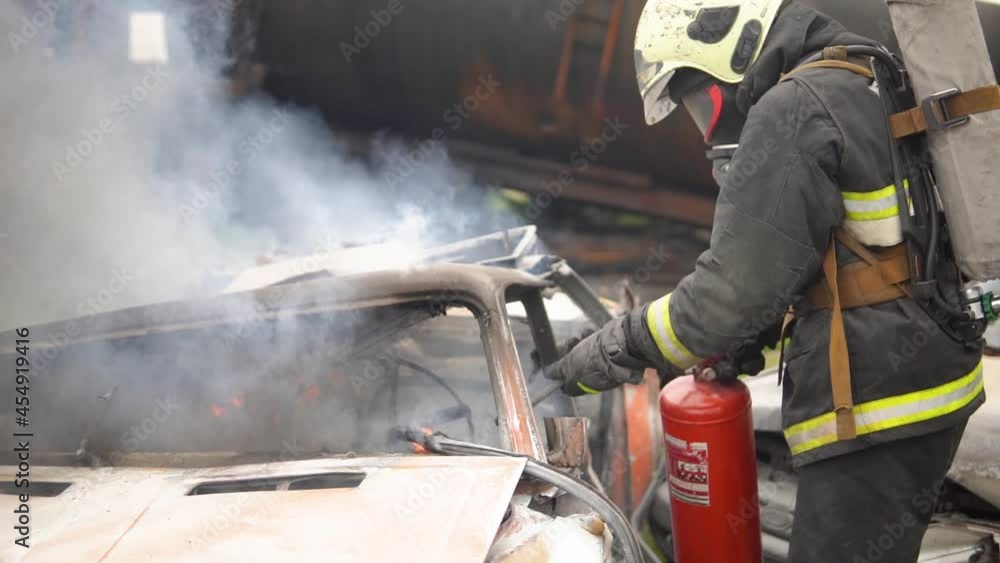 On the Car Crash Traffic Accident Scene: A fire rescue worker professionally extinguishes a fire in a car with a fire extinguisher. A lot of fire and smoke. Unblocking of victims. First aid services On the Car Crash Traffic Accident Scene: A fire rescue worker professionally extinguishes a fire in a car with a fire extinguisher. A lot of fire and smoke. Unblocking of victims. First aid services