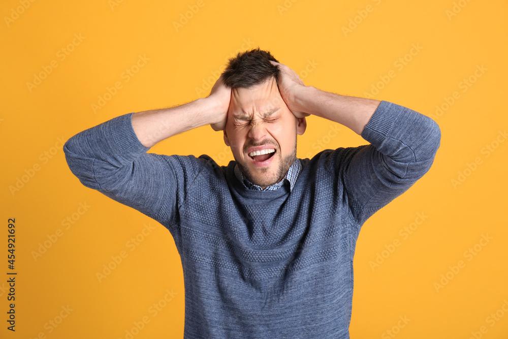 Man suffering from terrible migraine on yellow background Man suffering from terrible migraine on yellow background