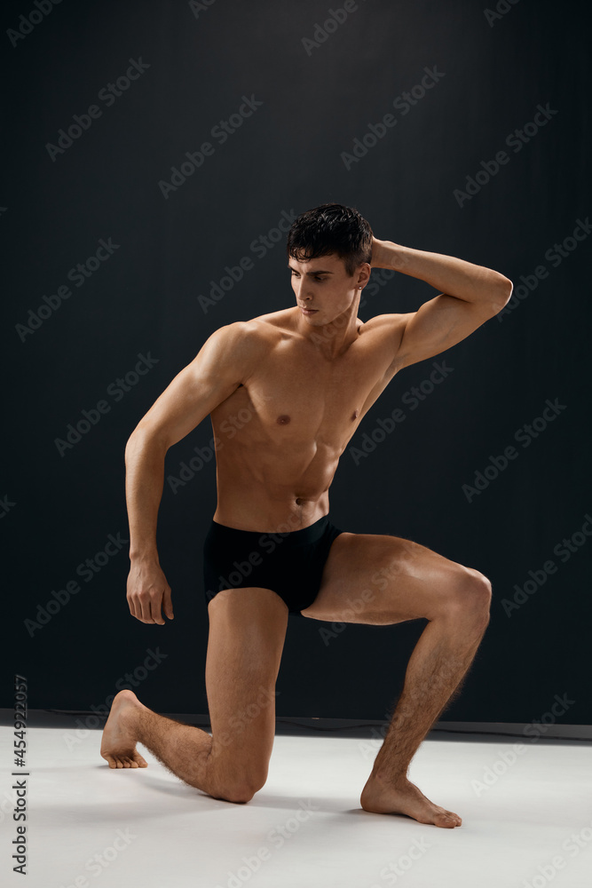 Obraz premium sexy man in black panties is kneeling with a pumped-up body studio