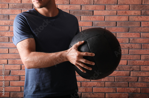 Athletic man with medicine ball near red brick wall, closeup