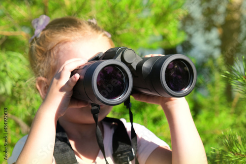 Little girl using binoculars in the forest. Exploring the world. Outdoor activities.