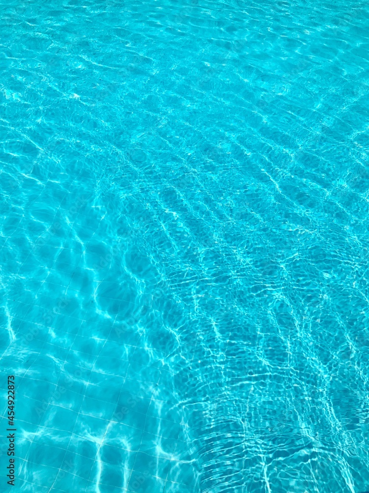 Bright blue clear transparent water in the swimming pool, the waves shine in the summer sunlight