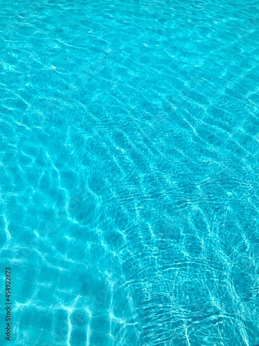 Bright blue clear transparent water in the swimming pool, the waves shine in the summer sunlight