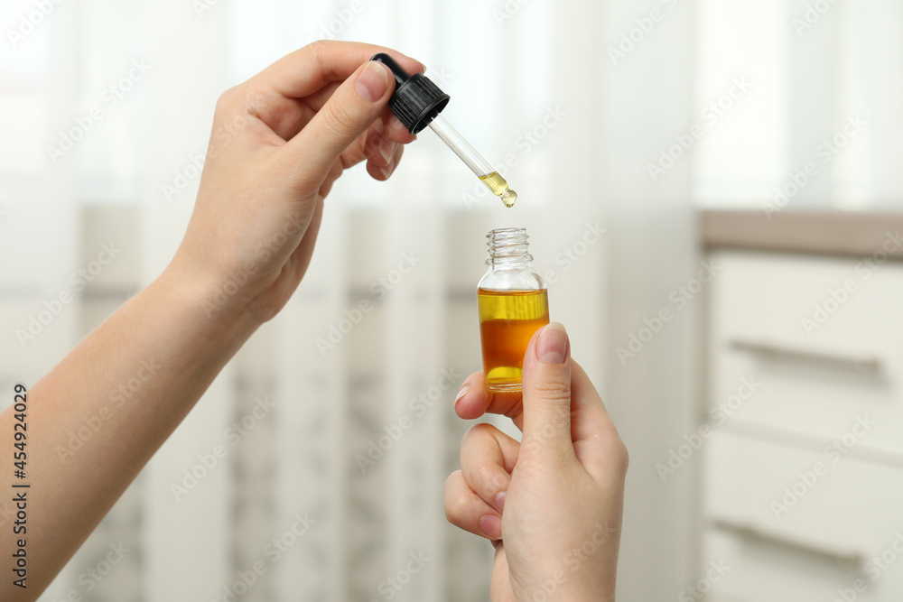 Woman holding bottle of hemp oil and pipette on blurred background, closeup Woman holding bottle of hemp oil and pipette on blurred background, closeup