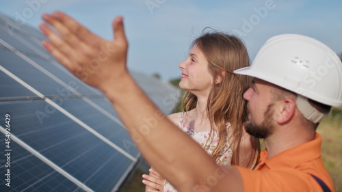 Father with little girl at solar power plant. The father talks about solar energy. The concept of green energy will save the planet for children. The father puts a protective helmet on the girl's head
