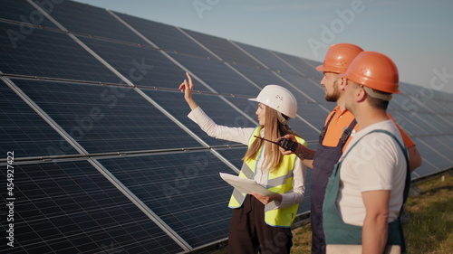 Three employees of alternative power plant walking and talking about scheme of solar panels. Team work. Group of specialists. Camera follows people. Meeting with the investor