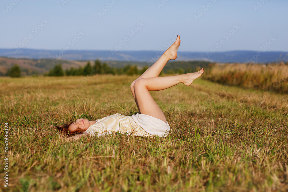 Happy girl lies on a field with mown grass and smiles. Photo of people outdoors in summer.