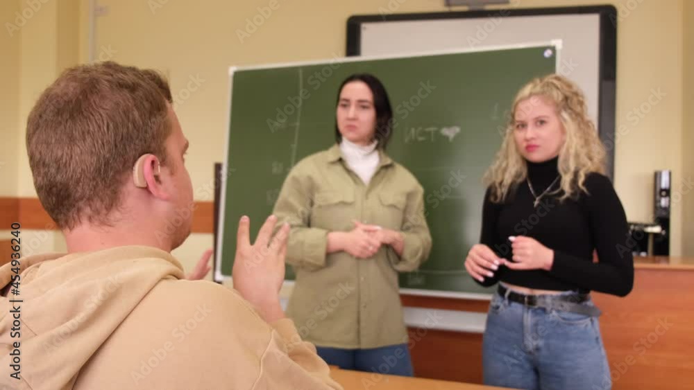 The girls and the guy are talking in Russian sign language. Three deaf students chatting in a university class The girls and the guy are talking in Russian sign language. Three deaf students chatting in a university class