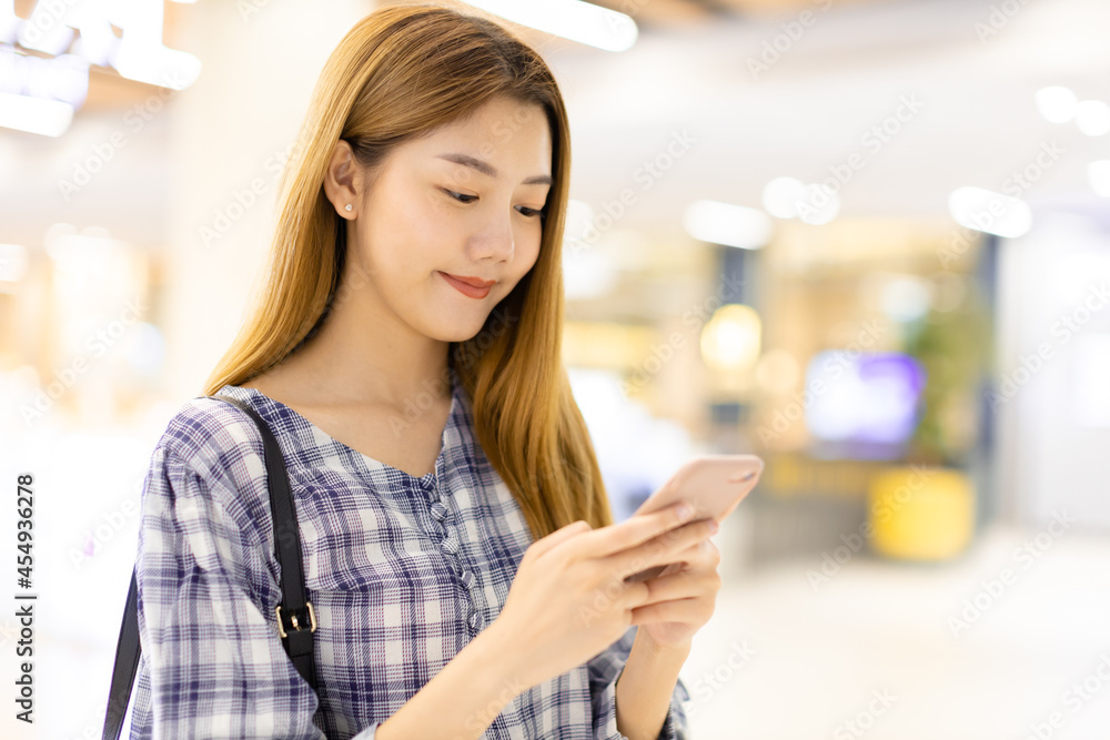 Smiling young Asian woman with shopping colour bags over mall background. using a smart phone shopping online and smiling while standing mall building. lifestyle concept Smiling young Asian woman with shopping colour bags over mall background. using a smart phone shopping online and smiling while standing mall building. lifestyle concept