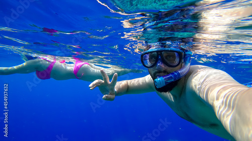 a bearded man in a mask and a breathing tube dives into the red sea against the background of a girl swimming behind him