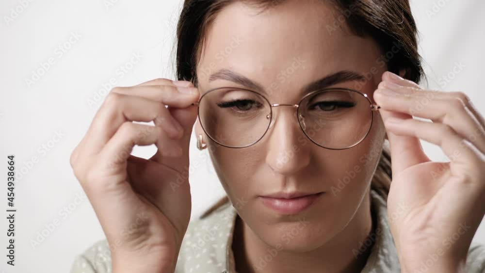 Woman puts on glasses. Positive woman on white background puts on glasses and smiles while looking at camera. Vision problems, student, teacher and education concepts Woman puts on glasses. Positive woman on white background puts on glasses and smiles while looking at camera. Vision problems, student, teacher and education concepts